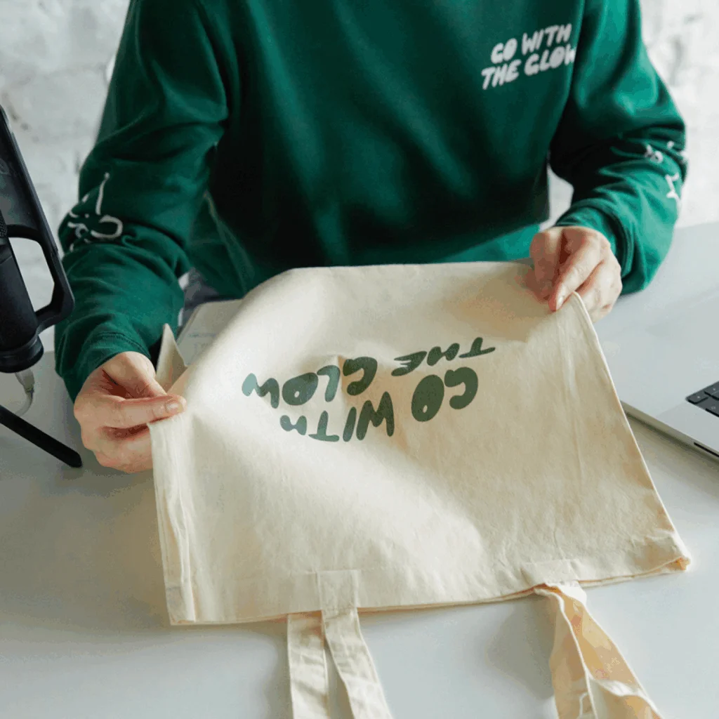 A woman is holding a custom “Go with the glow” tote bag.