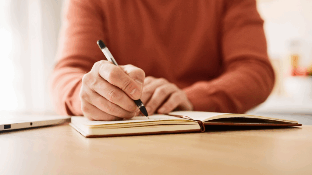 A man writing in a notebook with a pen, focused on his task in a well-lit environment.