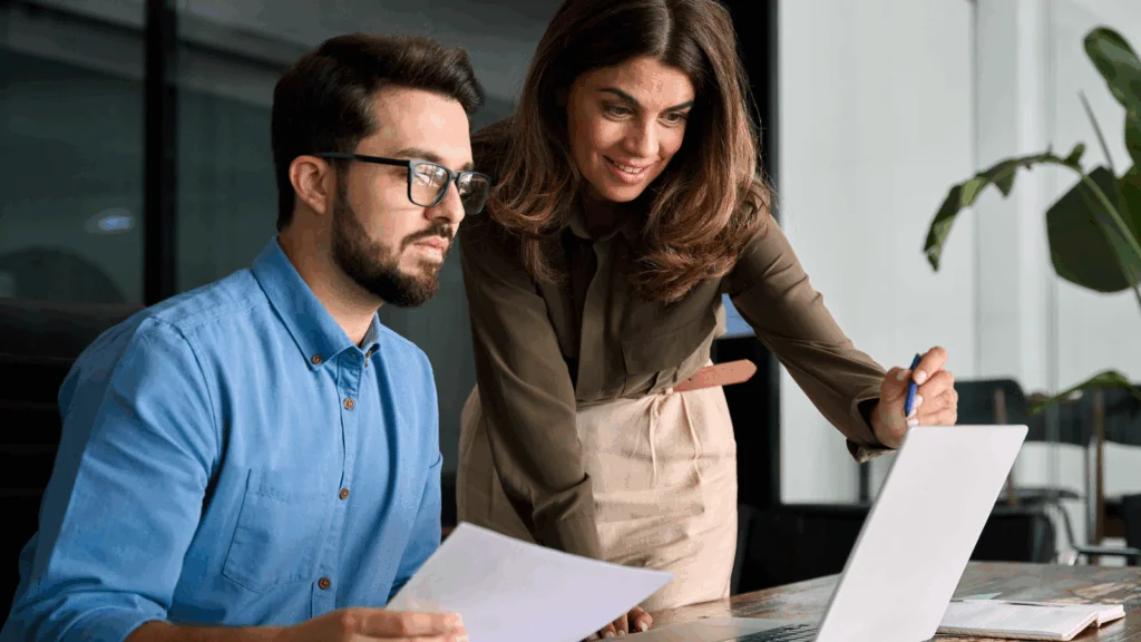 A man and woman collaborating on a laptop, focused on their work in a modern office setting.