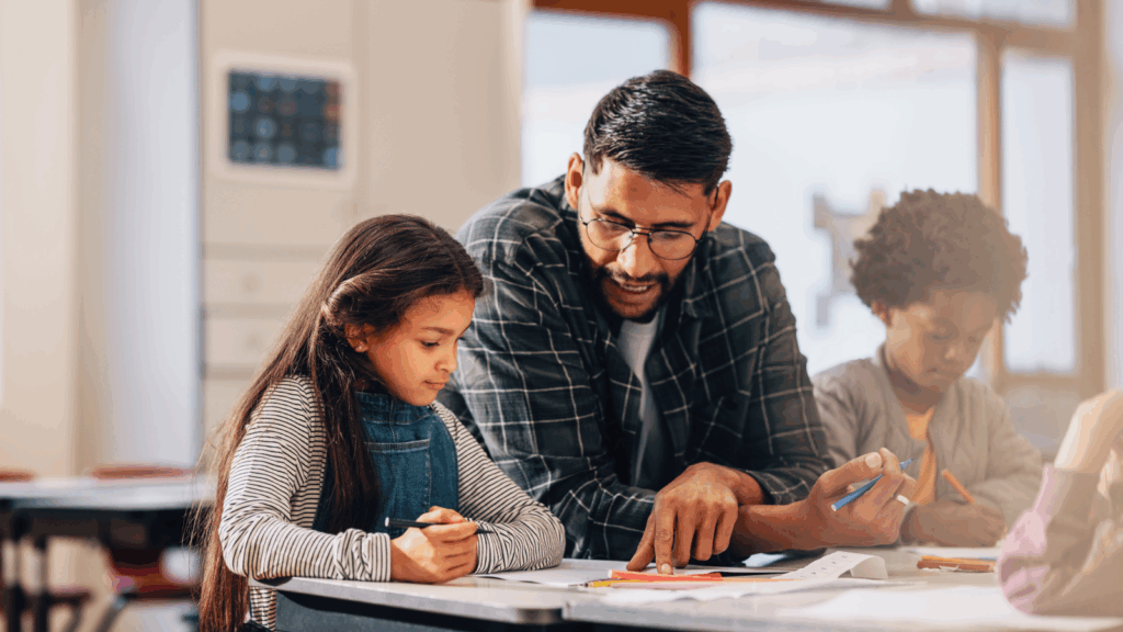 A man assists two children with their homework at a table, surrounded by books and school supplies.