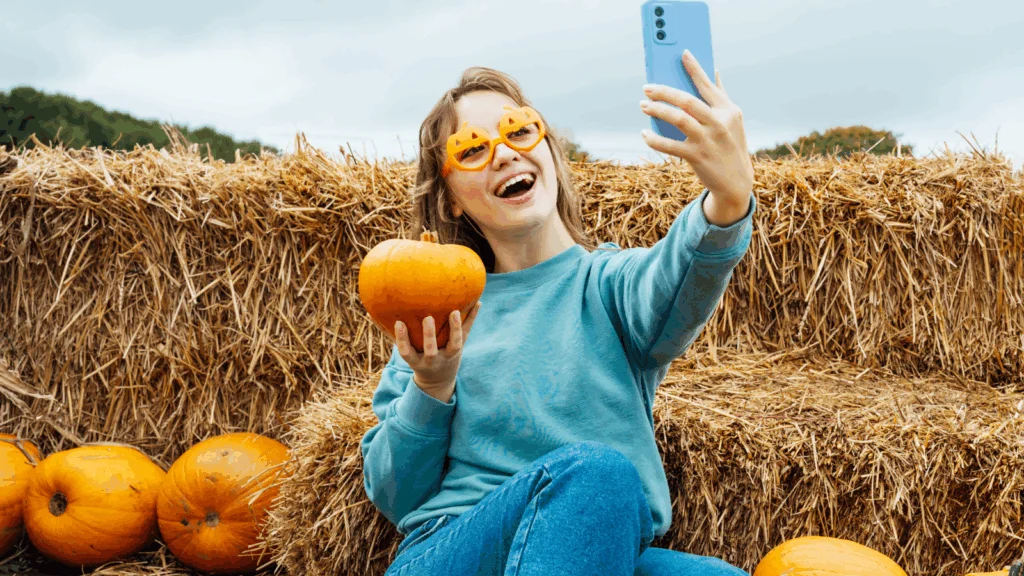 A woman social media influencer is taking a picture with Halloween pumpkins.