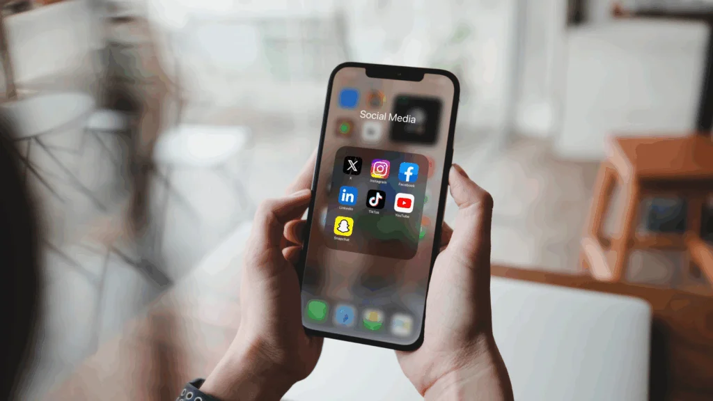 A person is holding a mobile phone with multiple social media app icons on the screen.