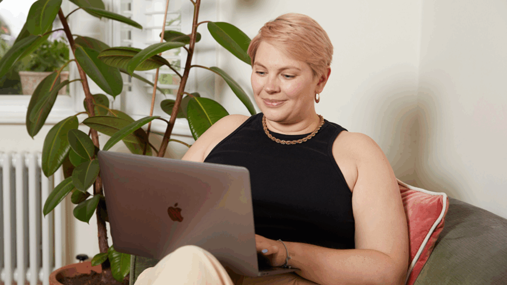A smiling woman is sitting in a chair with a laptop, selling art on eBay.