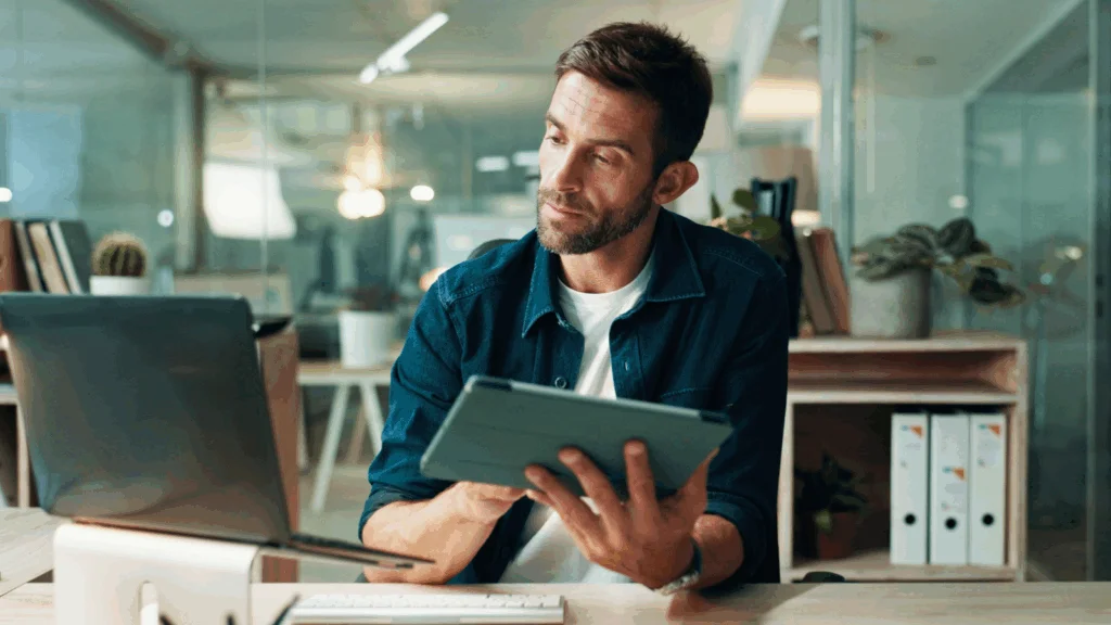 A man sits at a desk, focused on a tablet computer in front of him.