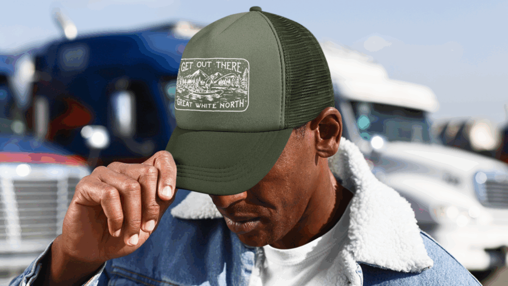 A man wearing a trucker hat and a green hat, smiling while standing outdoors in a casual setting.