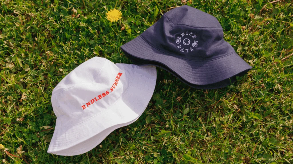 Two colorful bucket hats resting on green grass beside a blooming dandelion.