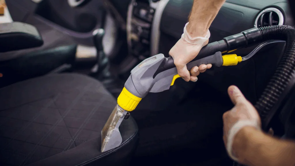 A person using a vacuum cleaner to clean a car seat, focusing on removing dirt and debris from the fabric.