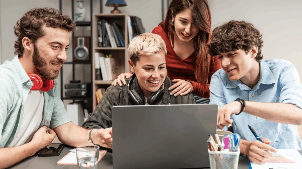 Content creation and education platforms Four young people gather around a laptop, intently focused on the screen as they discuss its content.