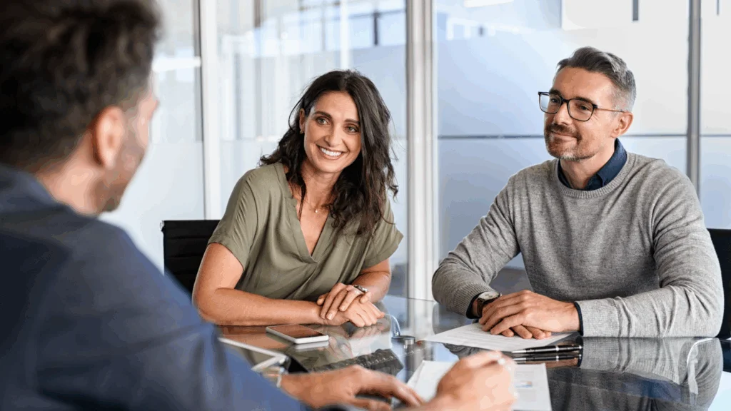 A man and woman sit at a table while a man reviews a document in front of them.