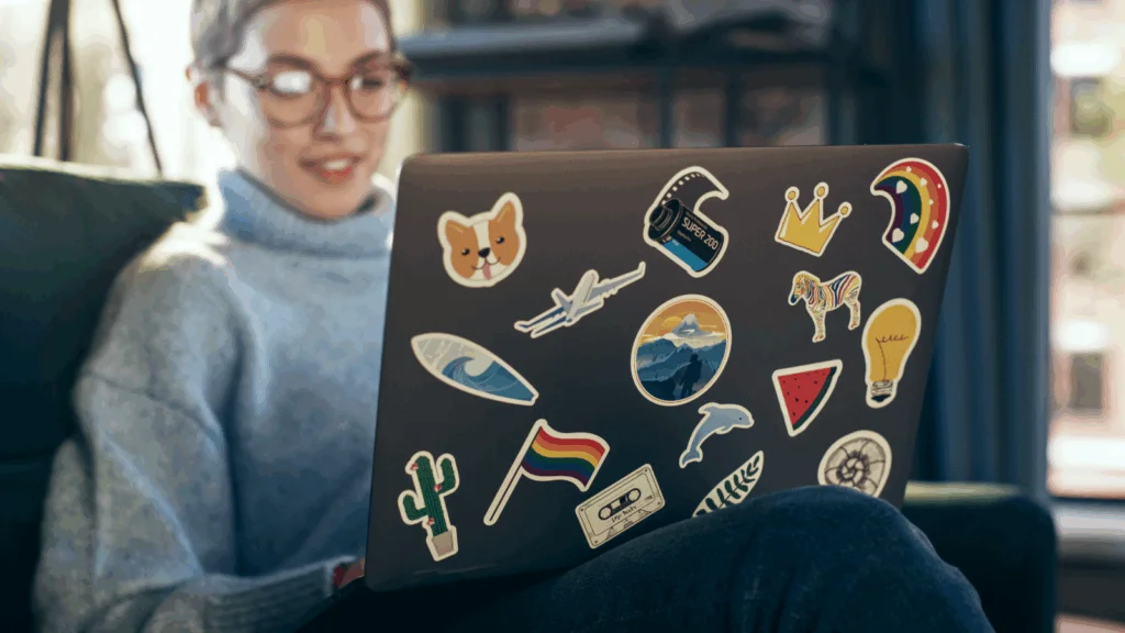 A woman sitting on a couch, using a laptop adorned with various colorful stickers.