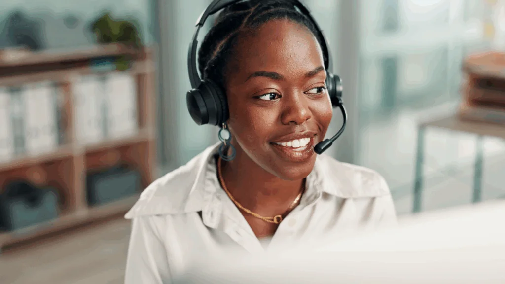 A woman with a headset smiles while working on a computer, focused and engaged in her task.