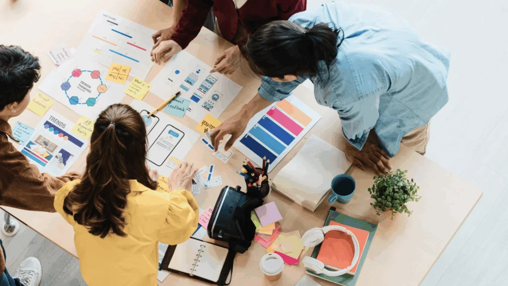 Several individuals engaged in teamwork, discussing ideas and reviewing materials for a project in a bright workspace.