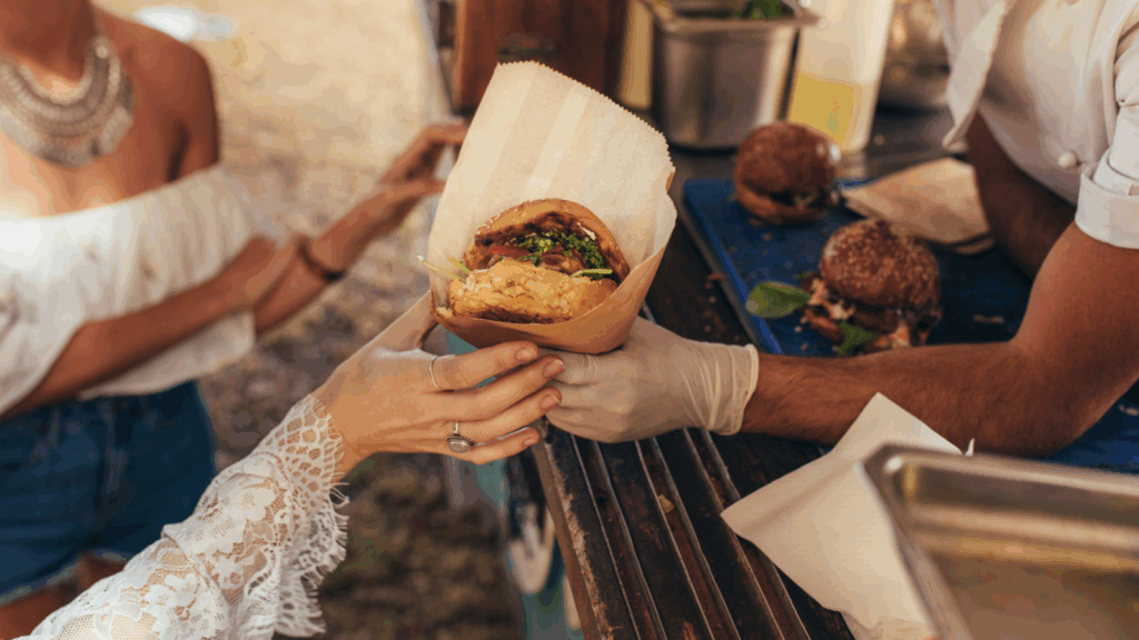 A man hands a sandwich to a woman at a food truck, showcasing a friendly interaction between them.