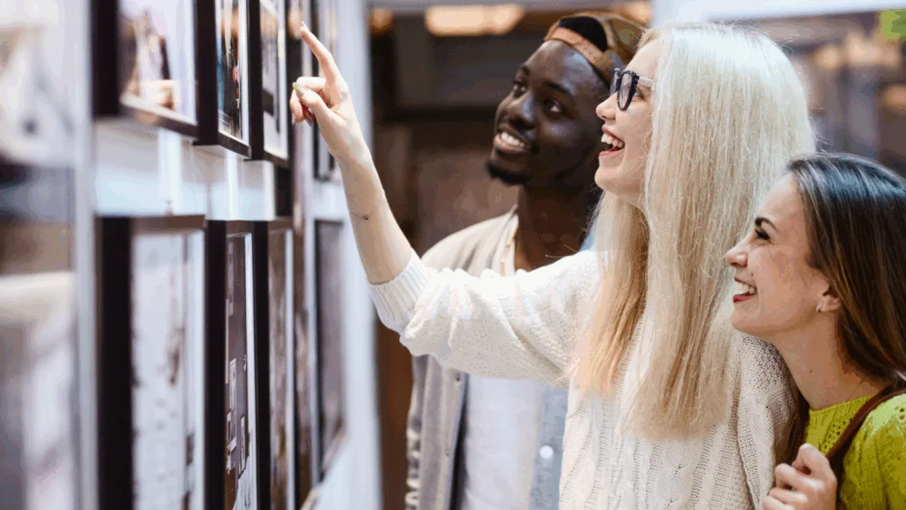 Three young people examining photographs displayed on a wall in an indoor setting.