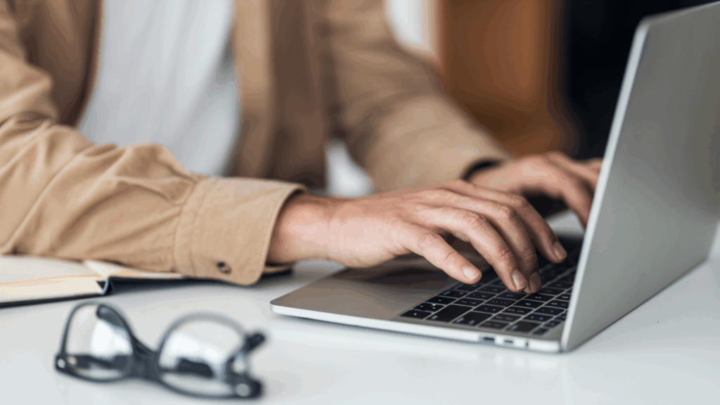 A person focused on typing on a laptop computer, with hands positioned on the keyboard.