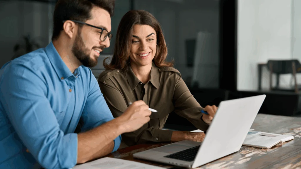 A man and woman smile at a laptop, sharing a moment of joy and engagement together.