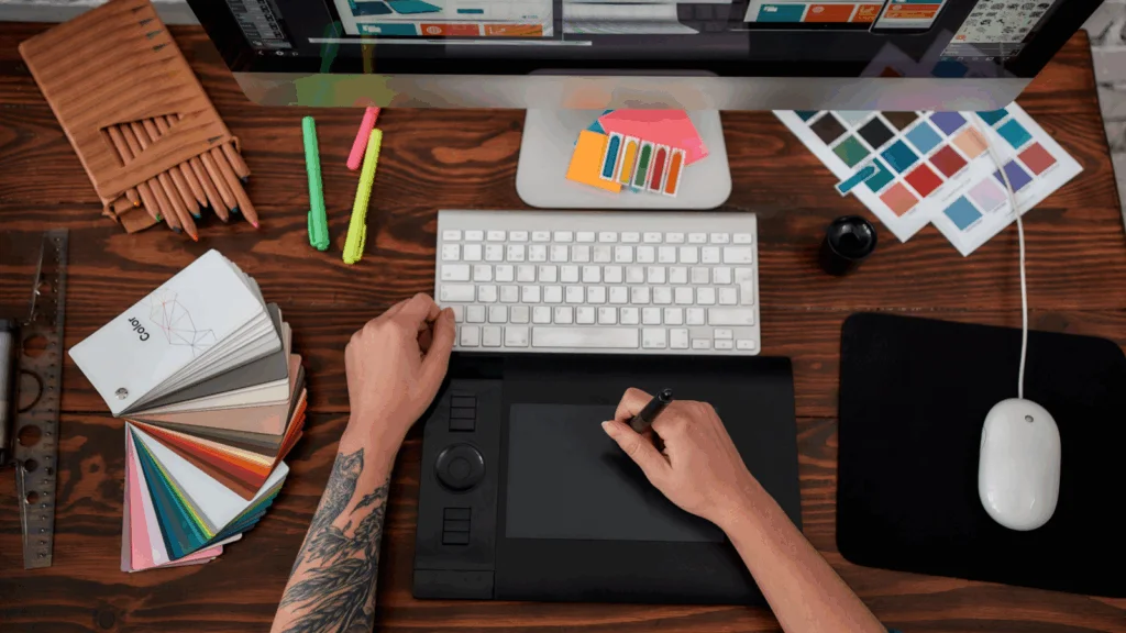 A person using a computer, holding a pen in one hand and a mouse in the other, focused on their work.