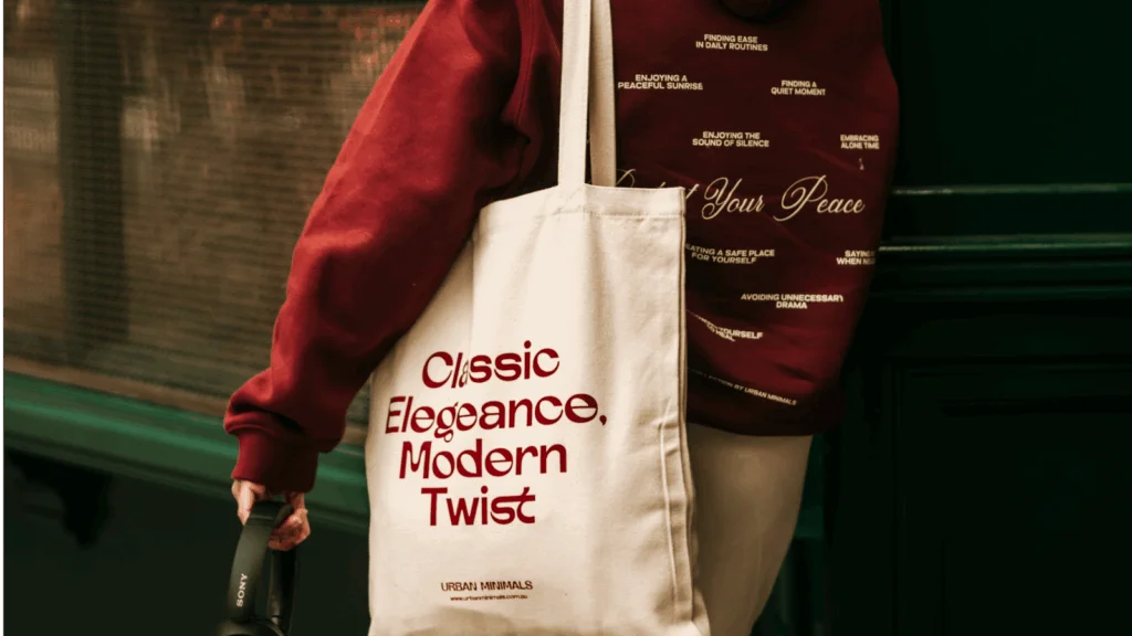A woman holds a tote bag featuring the phrase "classic essence modern twist" in a stylish font.