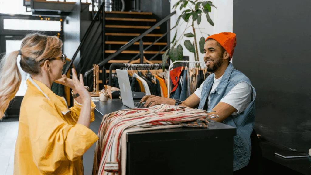 A man and woman engage in conversation while browsing clothing in a retail store.