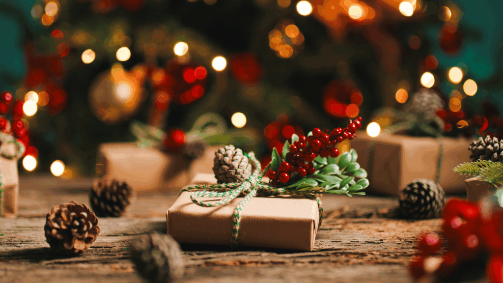 A collection of colorful Christmas gifts on a wooden table, illuminated by twinkling Christmas lights in the background.