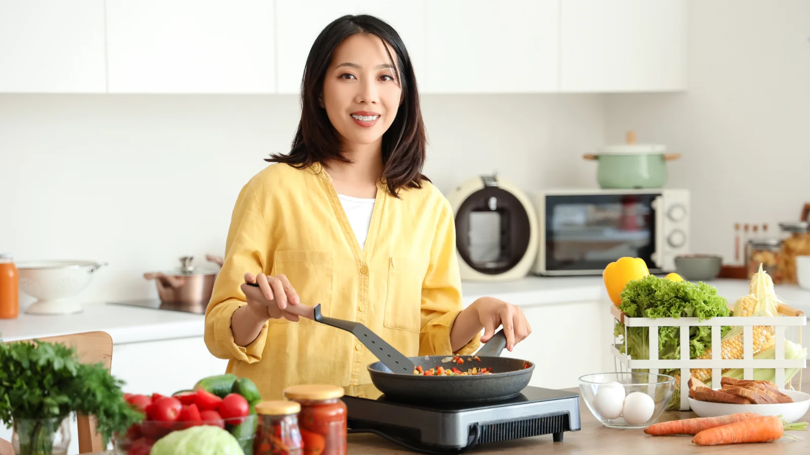 A woman preparing a meal in a kitchen, surrounded by fresh vegetables on the countertop.