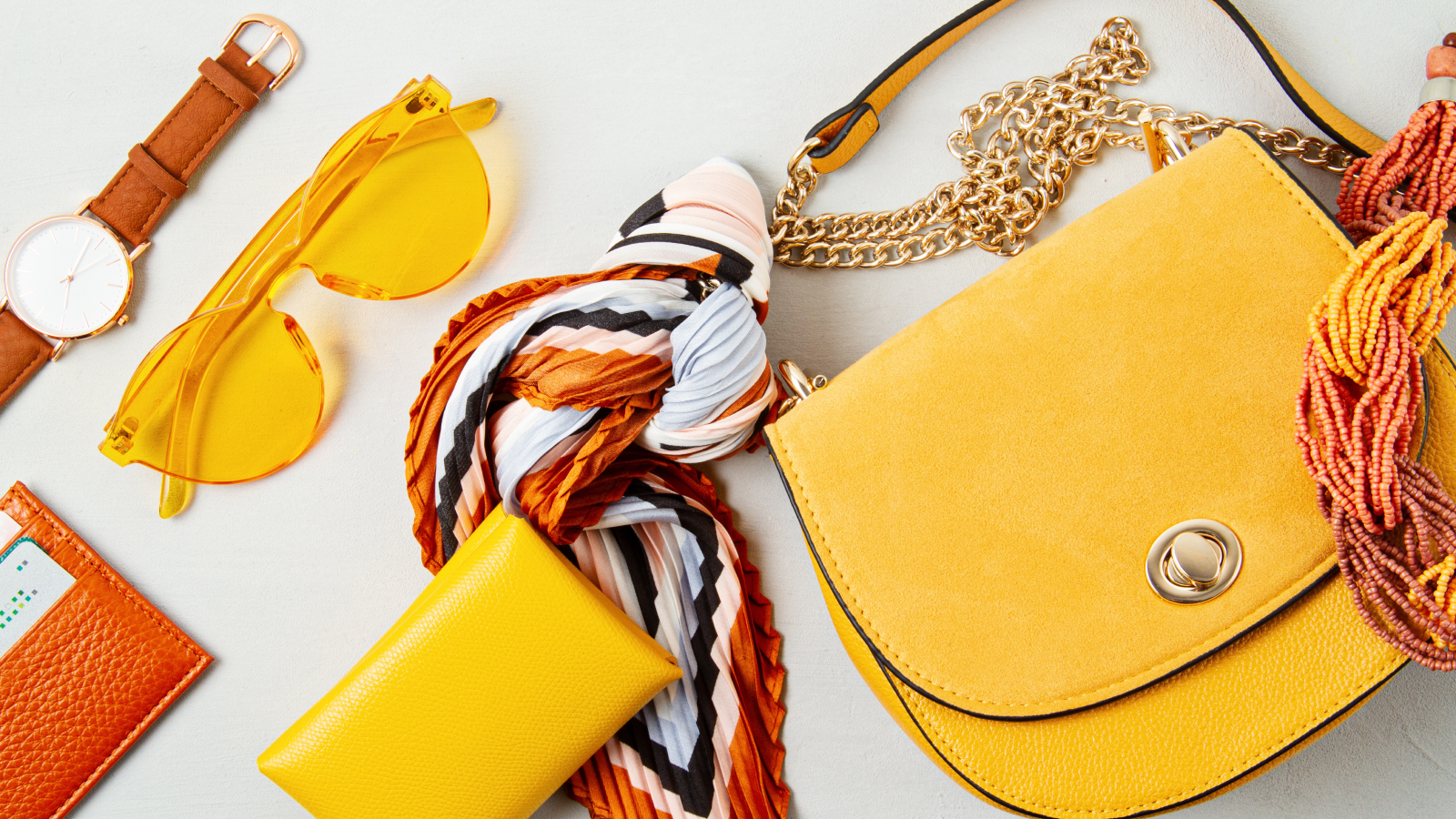 A yellow purse accompanied by sunglasses and various accessories arranged on a flat surface.