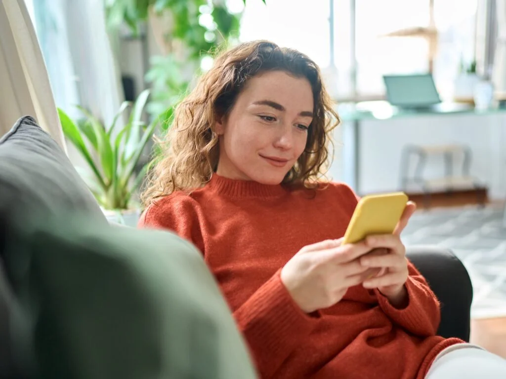 A woman sitting on a couch, focused on her phone, with a relaxed expression