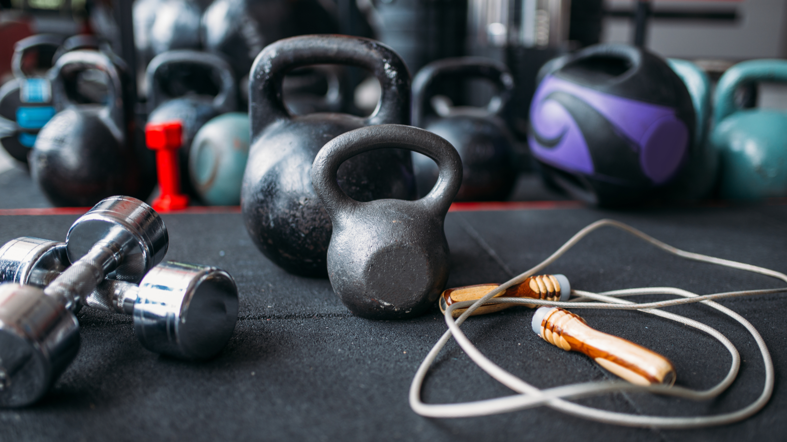 A selection of kettlebells and dumbbells arranged on a black surface, showcasing various weights and styles.