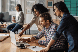 A group of diverse individuals collaborating on a laptop in a modern office setting