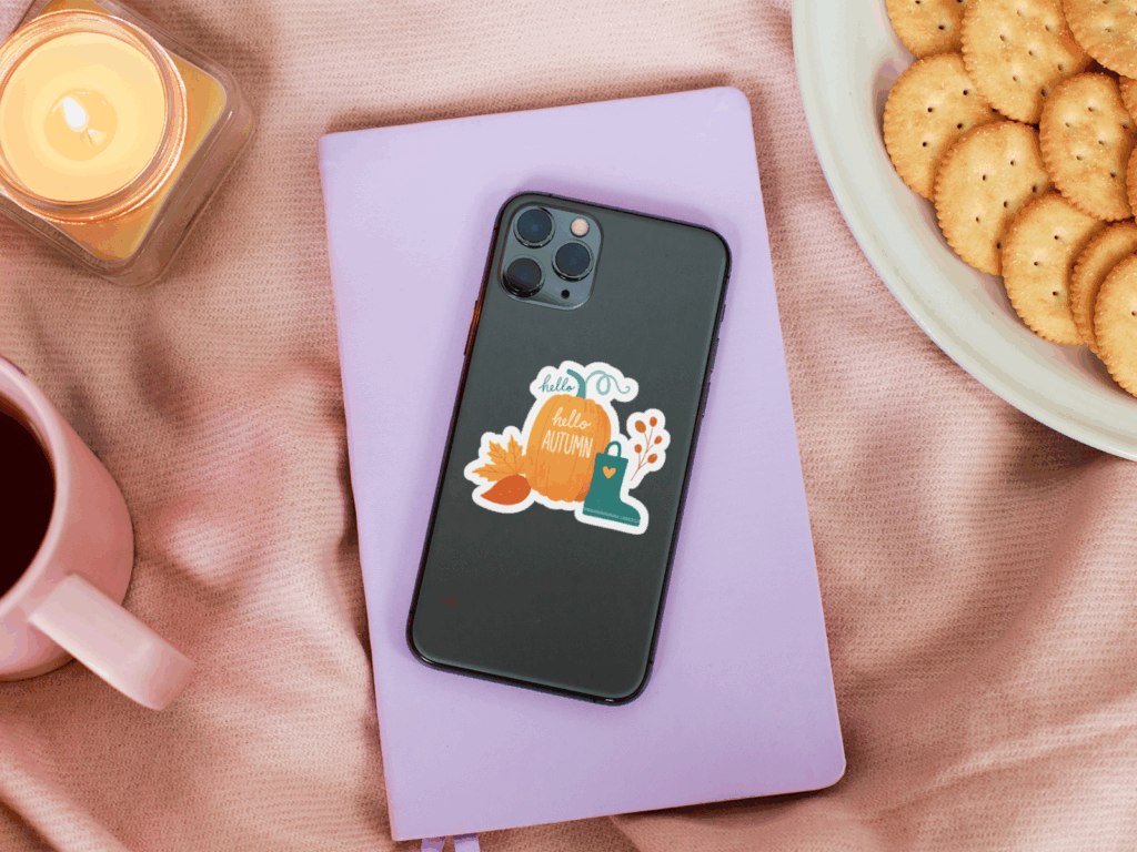 A phone with a sticker beside a cup of coffee and a plate of cookies on a table