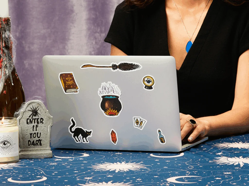 A woman sitting at a table with a laptop, surrounded by colorful stickers, focused on her work