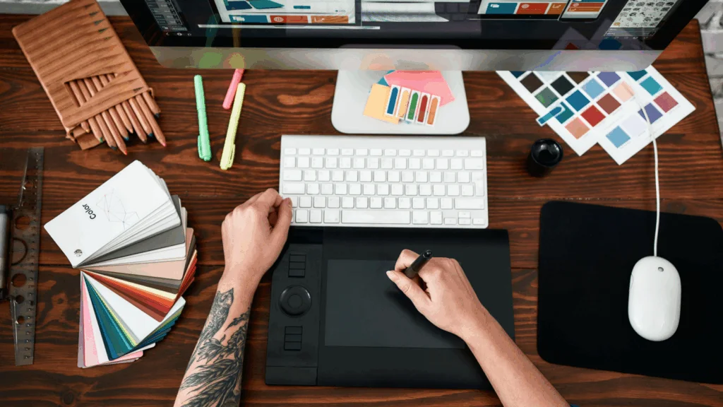 A person using a computer, holding a pen in one hand and a mouse in the other, focused on their work.