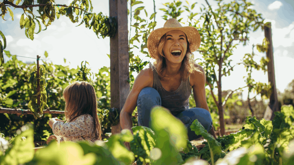 A woman and a child tending to plants in a vibrant organic garden filled with greenery and colorful flowers.