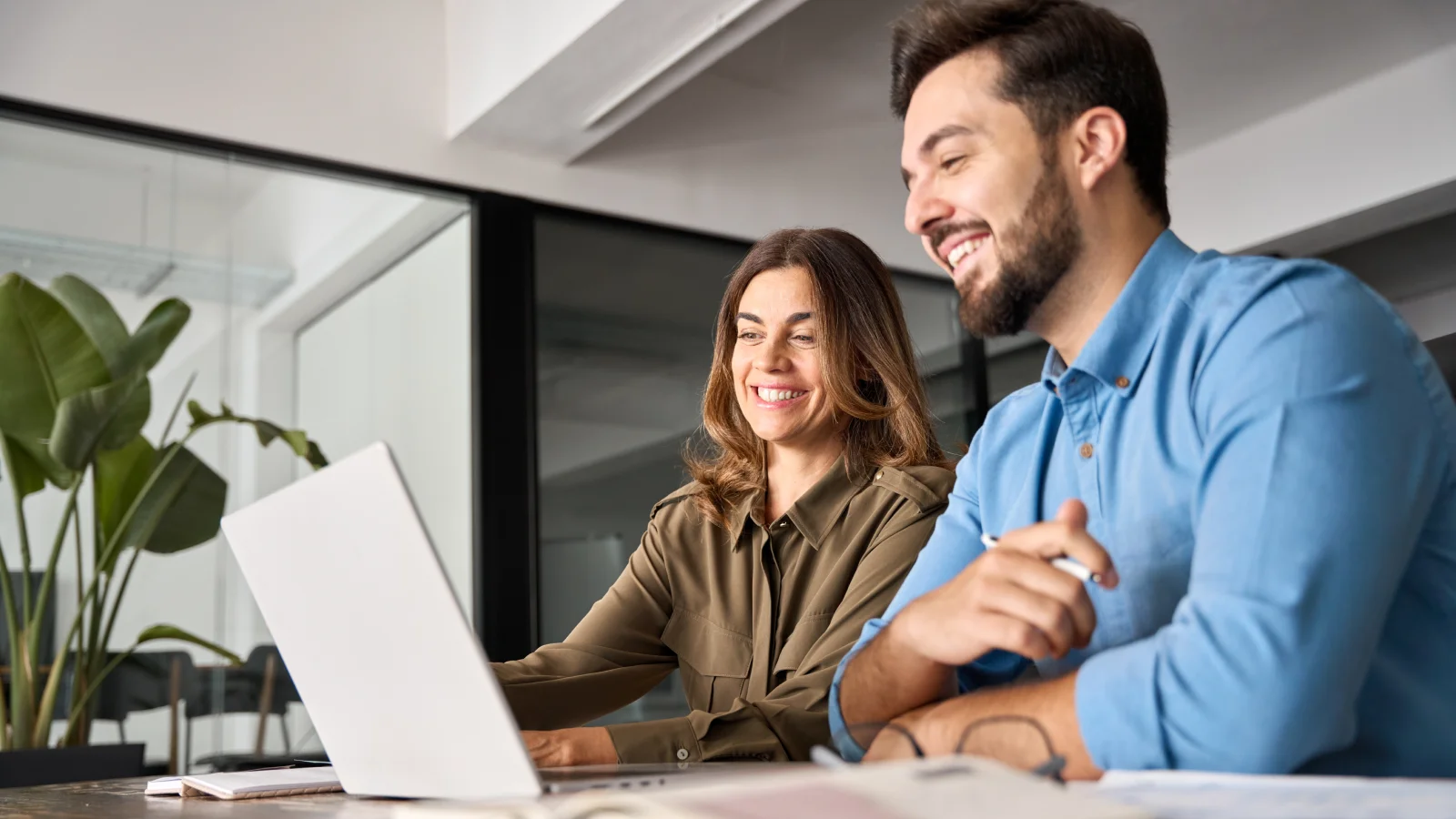 A man and woman smile while seated at a desk, conveying a sense of collaboration and positivity.
