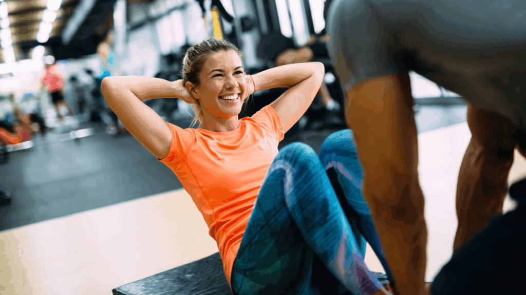 A smiling woman sits on a mat in a gym, exuding positivity and confidence during her workout session.