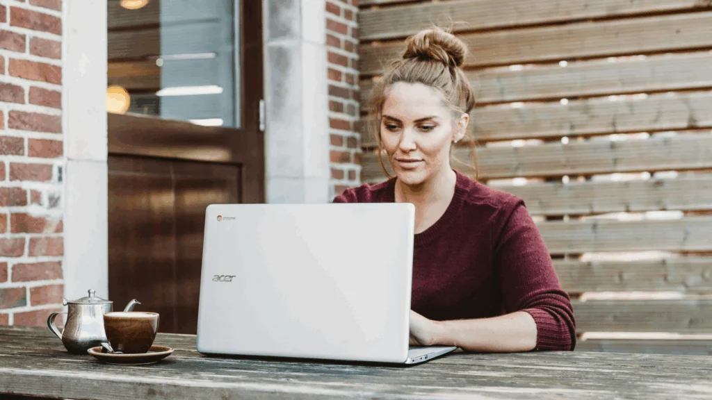 A woman seated at a table, focused on her laptop, with a calm expression in a well-lit room.