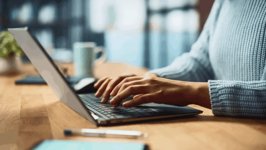 Website and page building Best Shopify apps A person focused on typing on a laptop computer, with hands positioned on the keyboard.