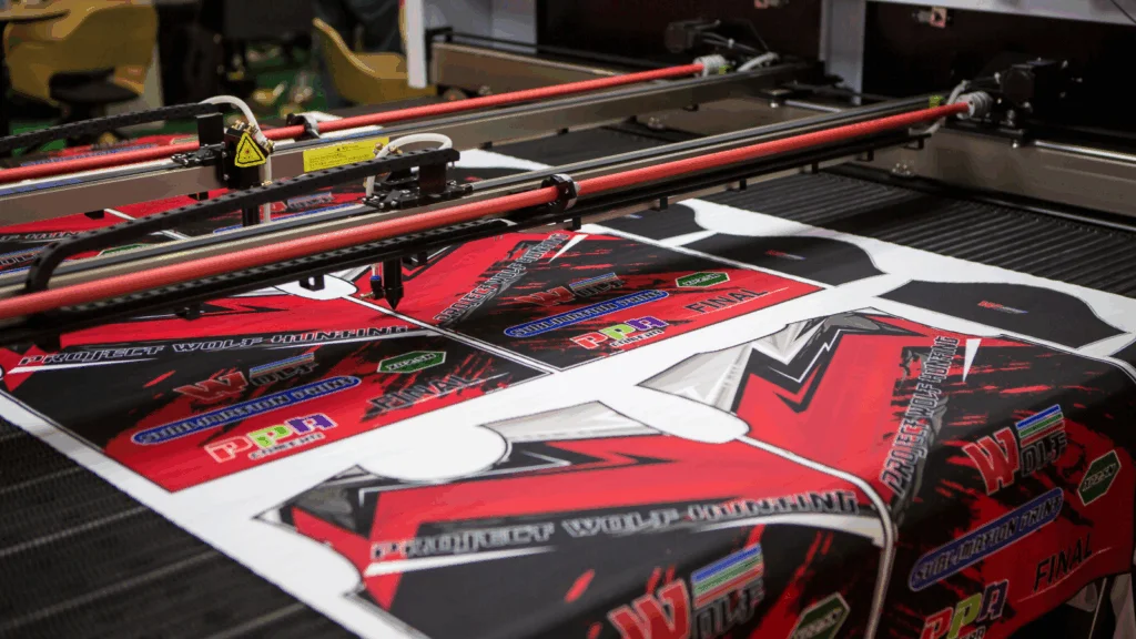 A dye sublimation printer processes vibrant red and black textile pieces featuring sporty designs and logos.