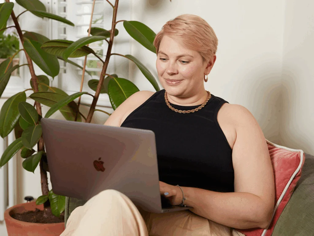A smiling woman with short hair sitting in a chair with a laptop, searching for the best blogging platforms to make money.