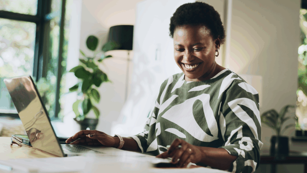 A smiling woman in a patterned shirt uses a laptop to start a print-on-demand puzzle business.