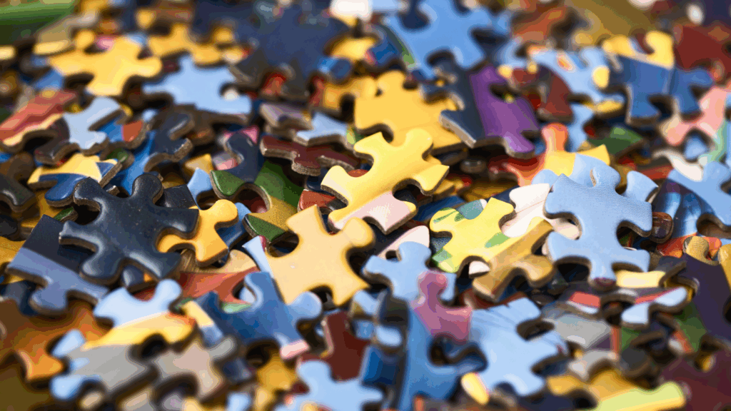 A close-up of scattered jigsaw puzzle pieces in various colors, including yellow, blue, and green.