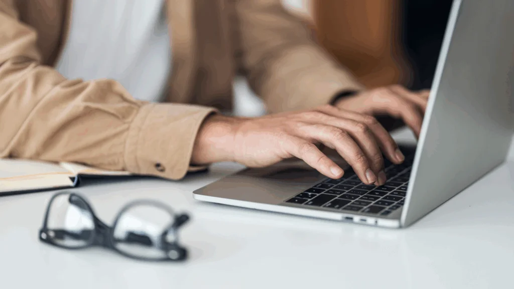 A person focused on typing on a laptop computer, with hands positioned on the keyboard.