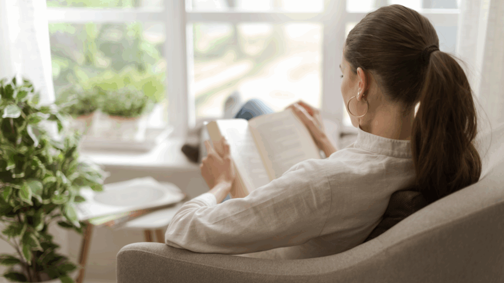 A woman sits in a chair, engrossed in reading a book, surrounded by a cozy atmosphere.