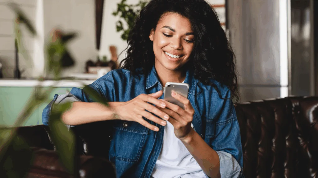 A woman wearing a denim shirt is focused on using her smartphone.