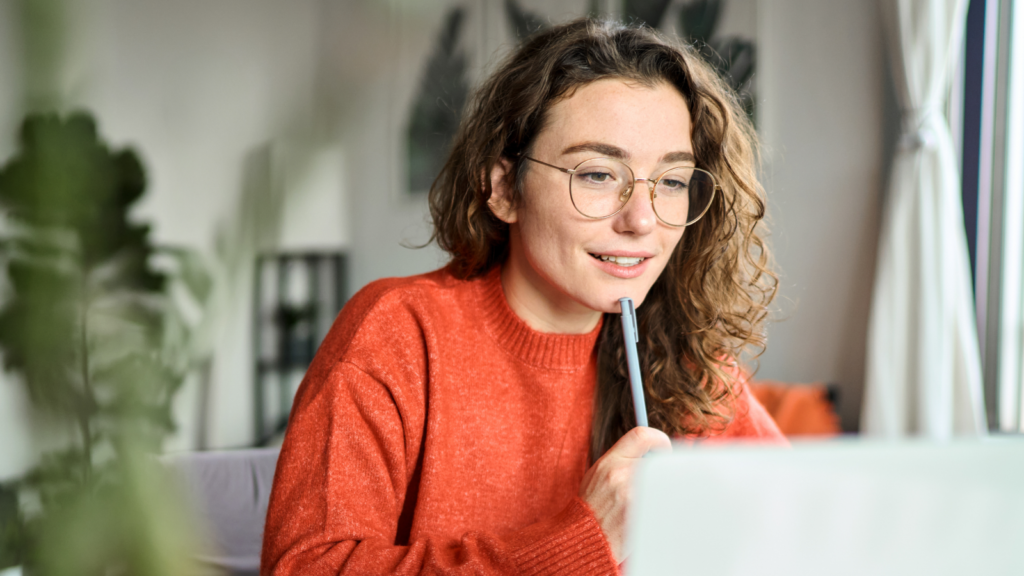 1 How to find trends on Etsy A woman wearing glasses is focused on her laptop screen, engaged in work or research.