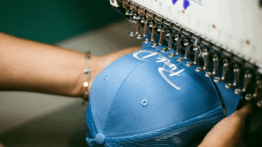 A person operates a sewing machine to create a hat, focusing on the fabric and stitching process.