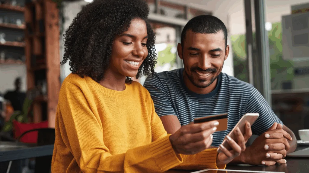 Man and woman using a credit card to pay at a coffee shop, with a cozy atmosphere and coffee drinks visible.