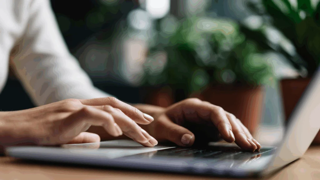 A person focused on typing on a laptop computer, with hands positioned on the keyboard.