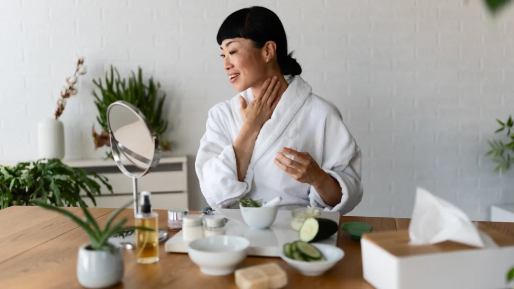A woman in a bathrobe sits at a table, resting her face in her hands, conveying a sense of stress or contemplation.