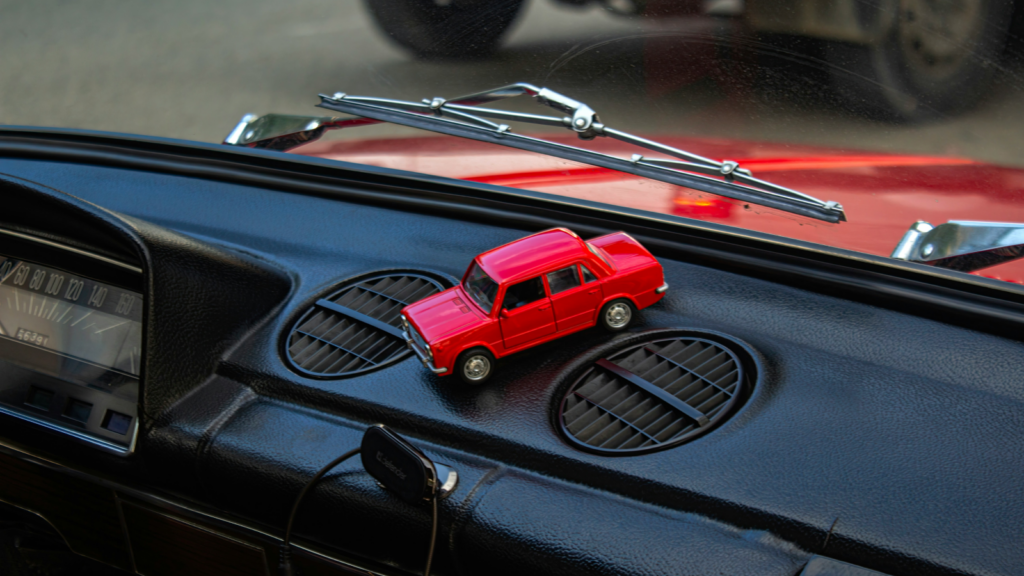 Car accessories A red toy car is placed on a car dashboard, showcasing its vibrant color against the interior setting.